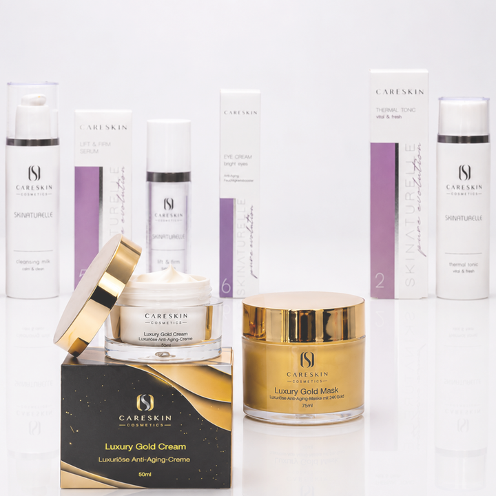 Premium-Pflegeset von CARESKIN Cosmetics auf weißem Hintergrund. Im Vordergrund stehen die Luxury Gold Cream und die Luxury Gold Mask mit goldfarbenen Akzenten. Im Hintergrund sind die Skinaturelle-Produkte Cleansing Milk, Lift & Firm Serum, Eye Cream und Thermal Tonic mit ihren Verpackungen arrangiert. Hochwertige Studioaufnahme mit spiegelnder Oberfläche und elegantem Kosmetik-Design.