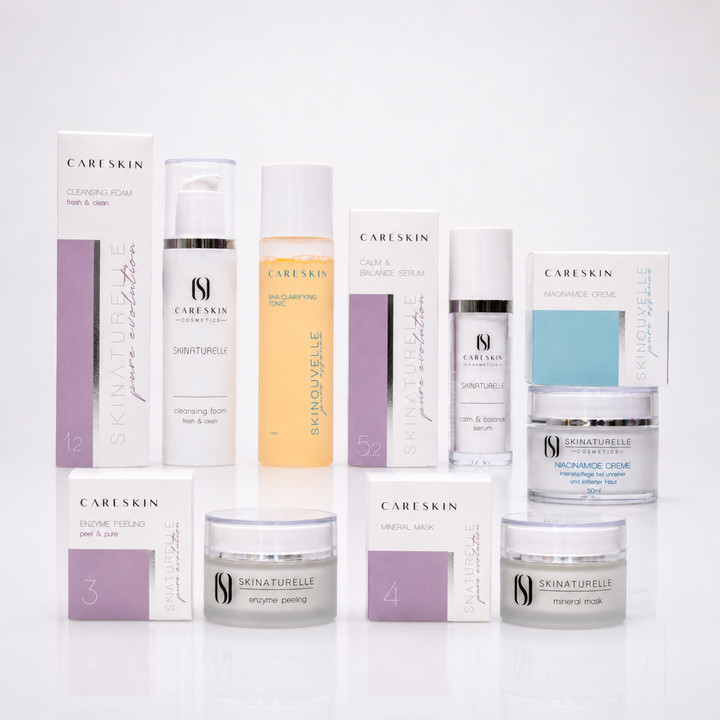 CARESKIN Hautpflegeset in einer hochwertigen Studioaufnahme auf weißem Hintergrund. Das Set umfasst Cleansing Foam, BHA Clarifying Tonic, Calm & Balance Serum, Enzyme Peeling, Mineral Mask und Niacinamide Creme mit ihren jeweiligen Verpackungen. Die Produkte sind harmonisch in zwei Reihen angeordnet und präsentieren das charakteristische CARESKIN-Design mit dezenten Flieder- und Türkisakzenten sowie einer leichten Spiegelung auf der glänzenden Oberfläche.